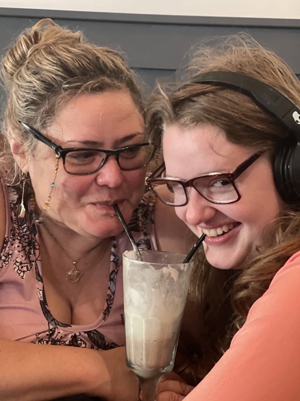 Faye and Mia cheek to cheek sharing a milkshake